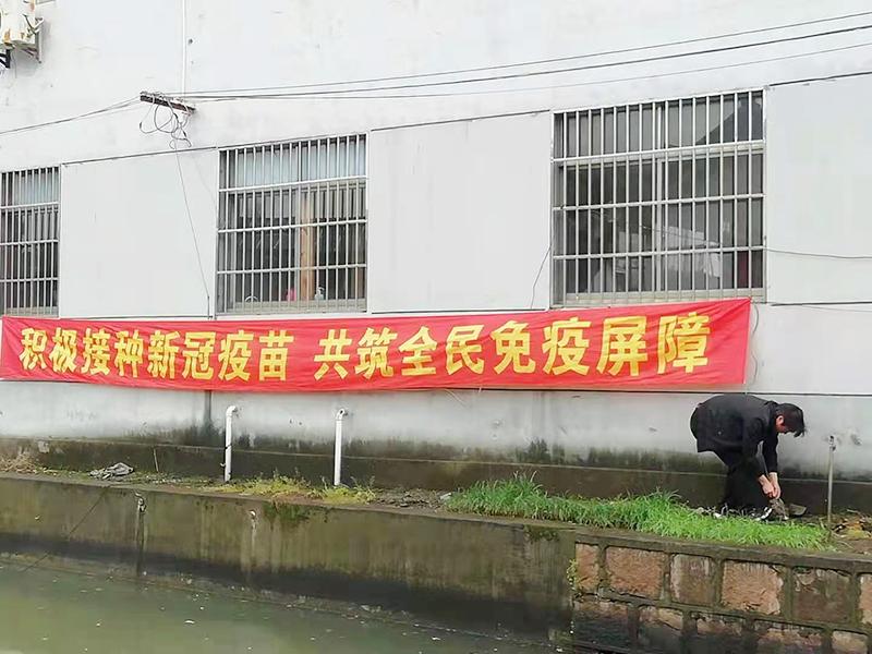 "积极接种新冠疫苗,共筑全民免疫屏障,这位正在冒雨弯腰拉横幅的年轻