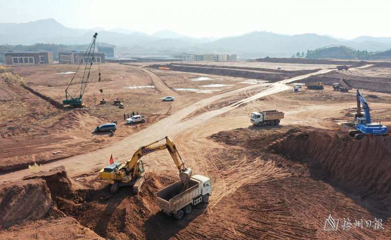 梅州综保区项目建设现场,挖掘机正在山坡上施工作业,运输车在来回穿梭