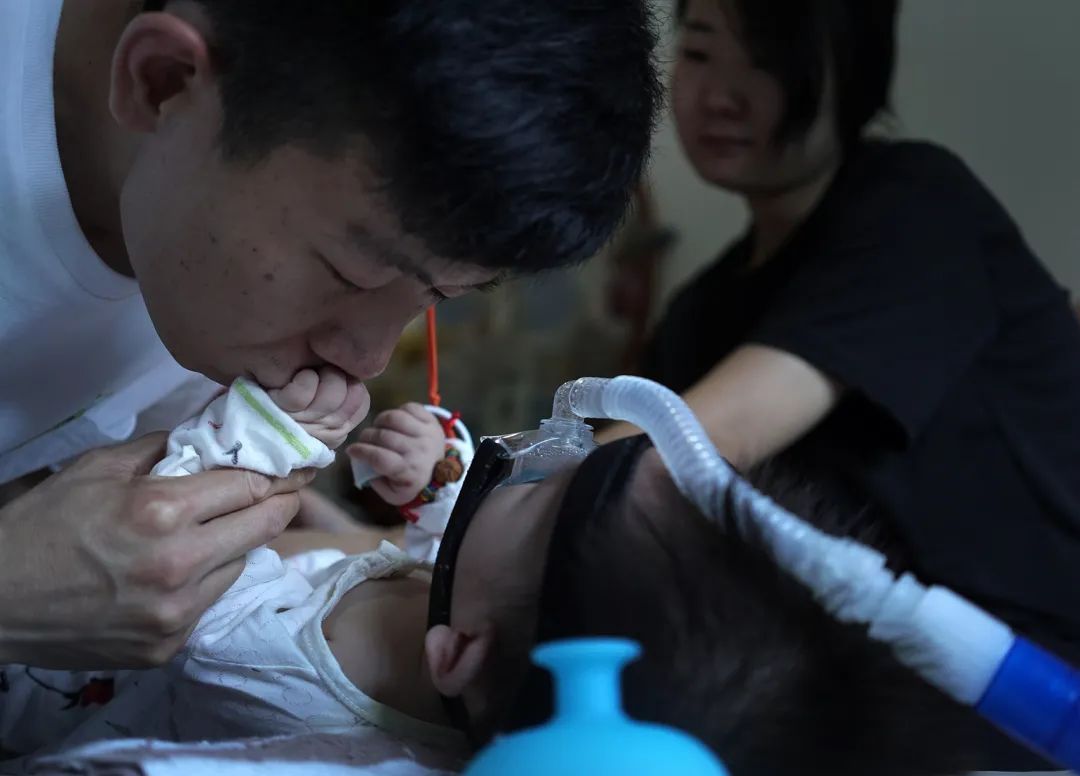 （2020年5月18日，福建厦门，32岁的黄根旺在亲吻孩子的手。他的孩子被确诊为SMA。图片来源/视觉中国）