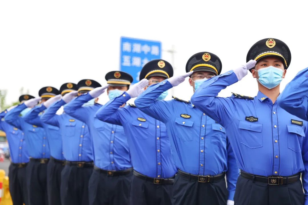 车队驶过,早已等候在道路两侧的城管队员们敬礼致意,环卫人员一边挥舞