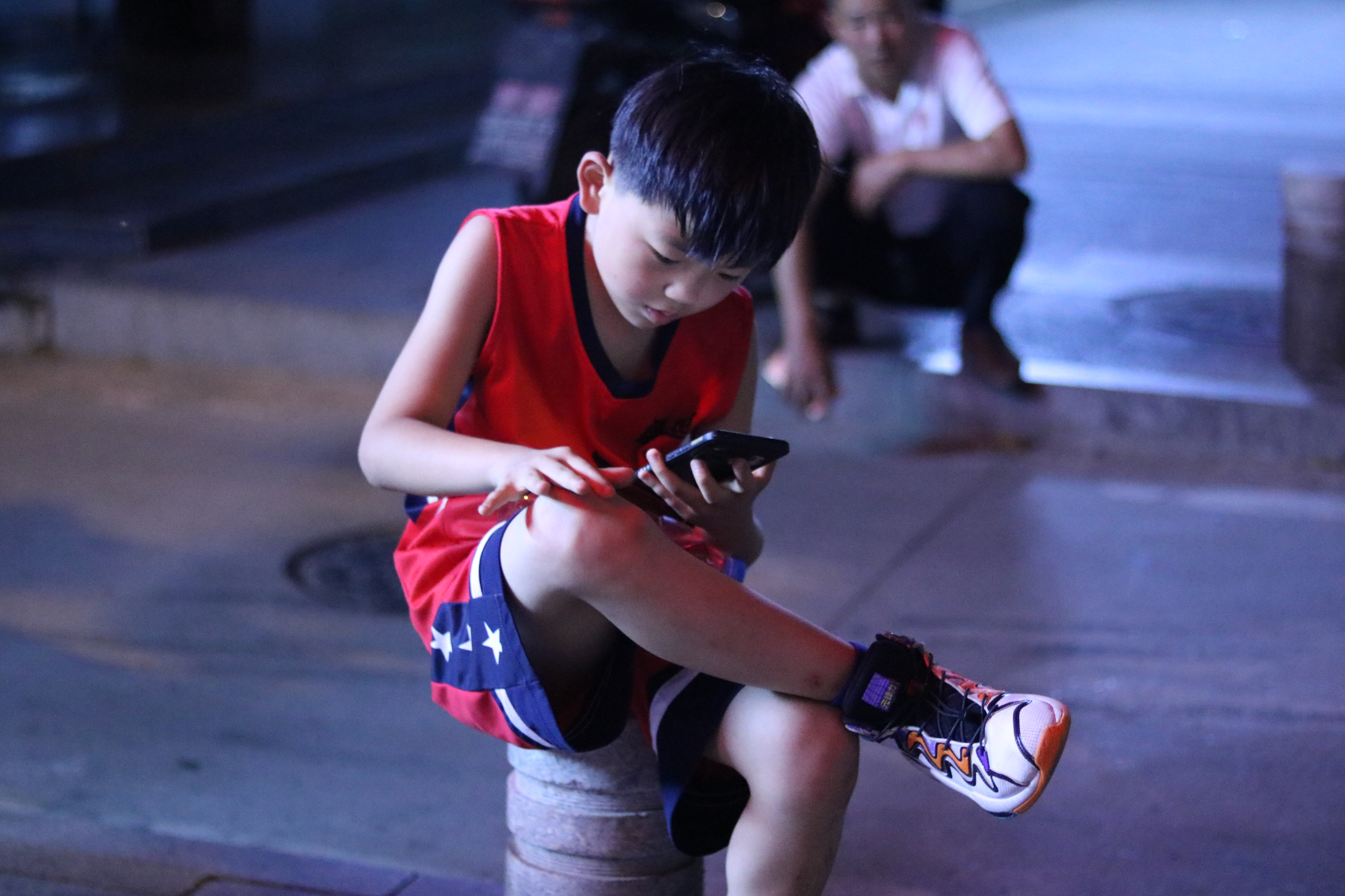 《移动社交正在成长》 一个小男孩正坐在路边石墩上玩手机