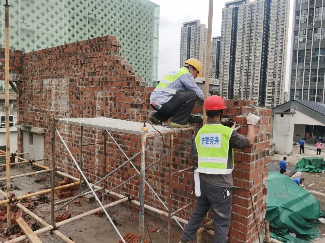 围墙边,已经砌起了2米多高的4堵红砖外墙,几名工人正站在脚手架上施工