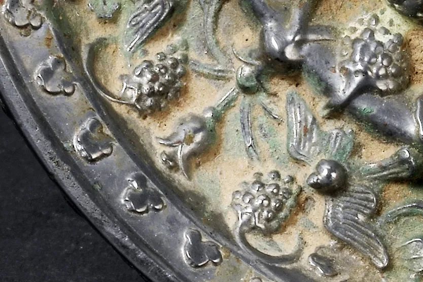 铜镜为圆形,兽形镜钮,以高浮雕瑞兽纹和葡萄纹为主题纹饰