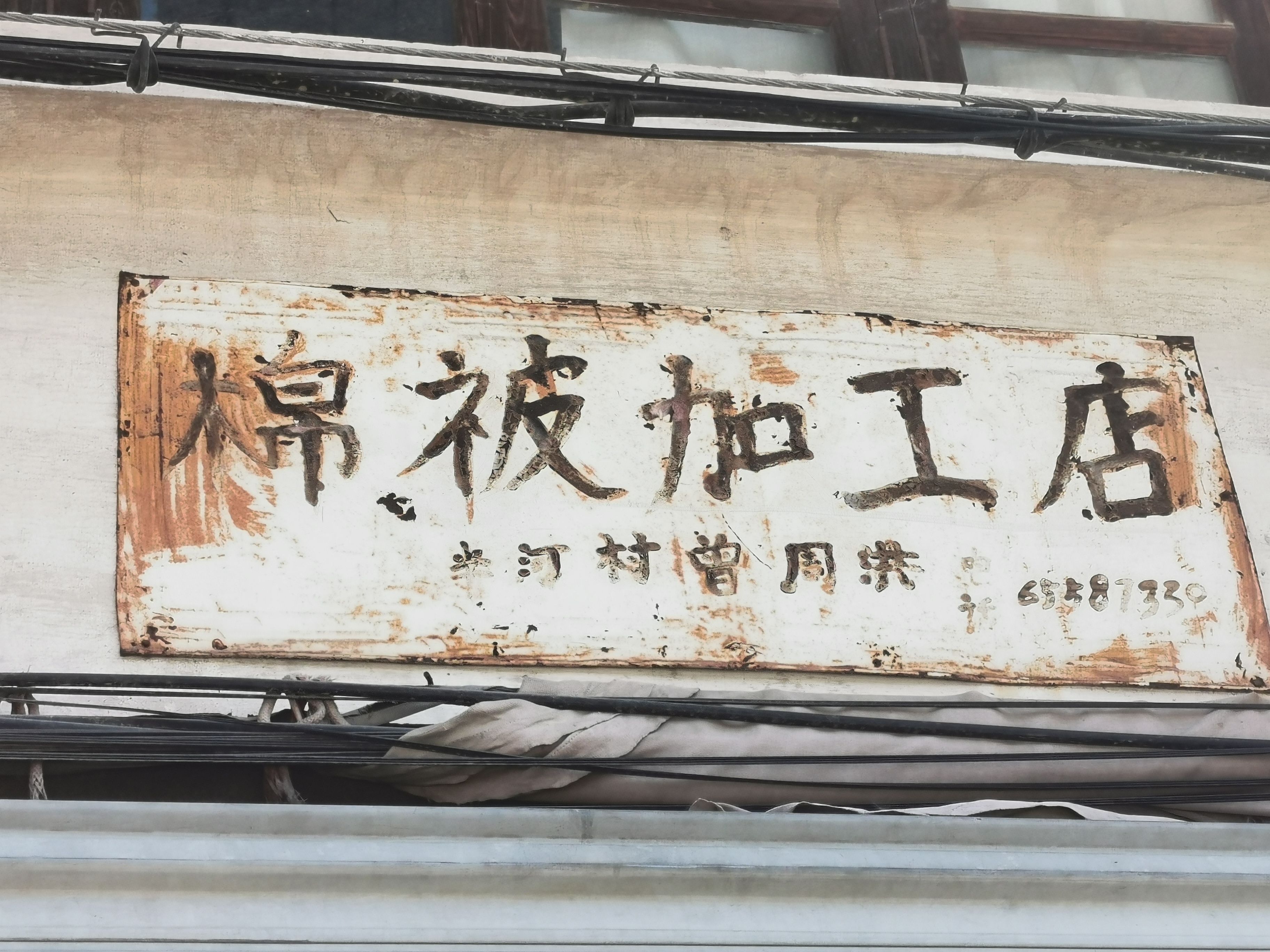 一间不起眼的民房上方挂着一方"广告牌",写有"棉被加工店""半河村曾周