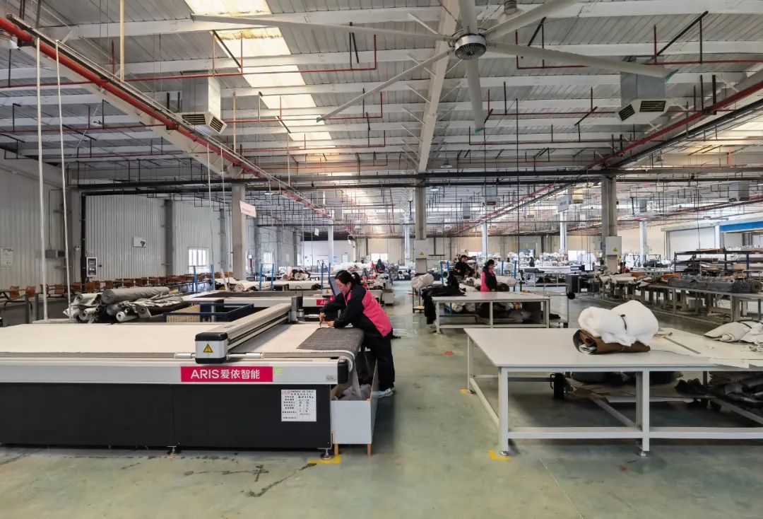 在数控裁剪车间,工人正在操作智能数控机床对沙发布料进行裁剪,上料