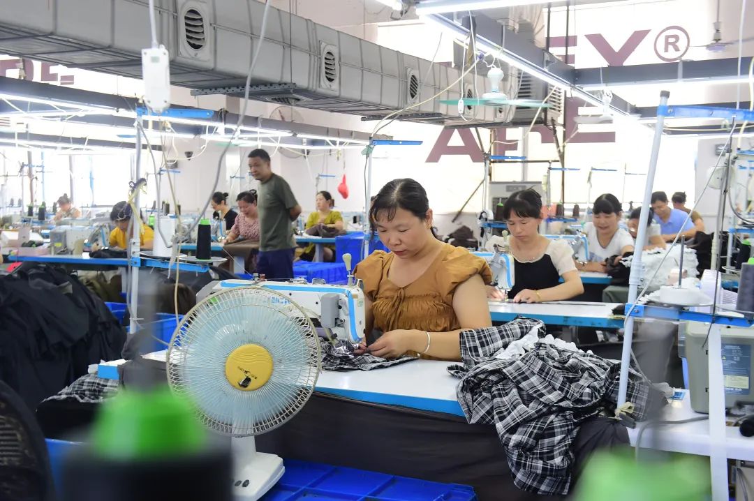 制衣车间内机器轰鸣,工人们分散在各自工位上验布,裁剪,缝制,整烫