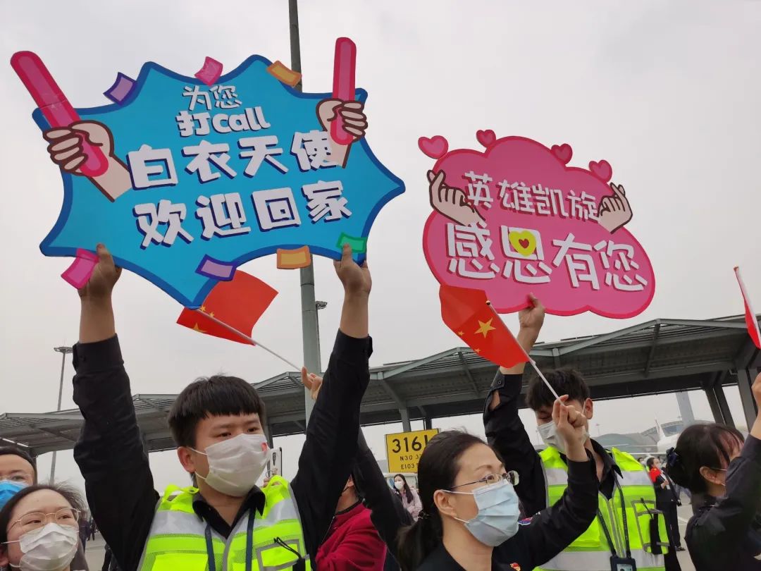 等待英雄凯旋手拿"向英雄致敬""欢迎回家"等标语列队欢迎的队员们欢迎