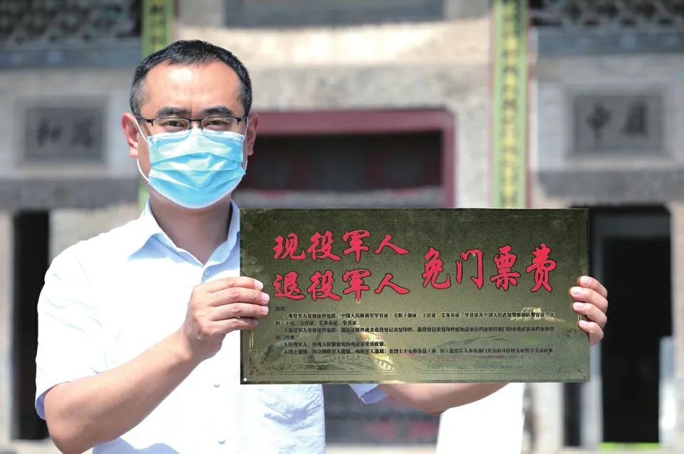 工作人员正在安装"现役军人,退役军人免门票费"标识牌,站在一旁观看的