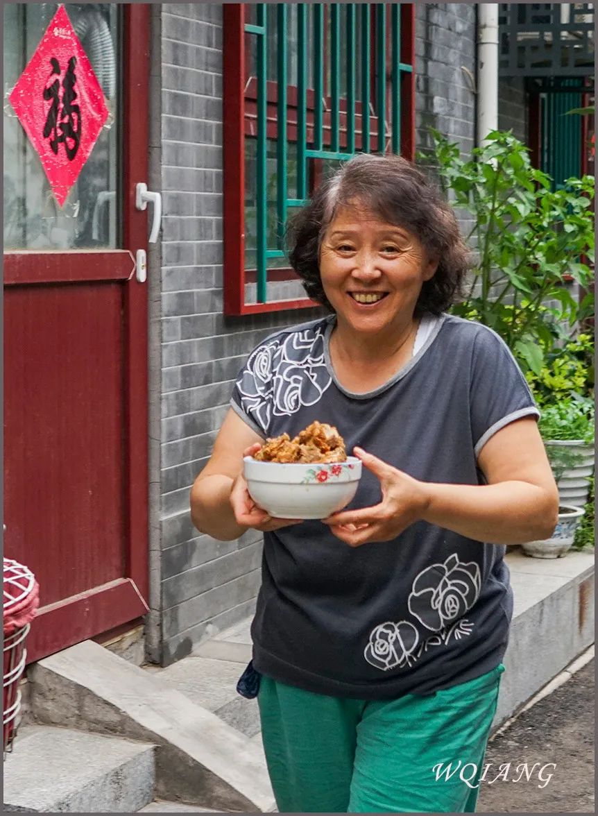 2016年,在前门附近胡同,大妈捧着一碗炖肉送给邻居.