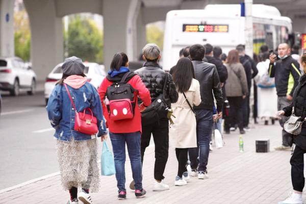 18日,乘客在18路公交车临河街站排队等候乘车.