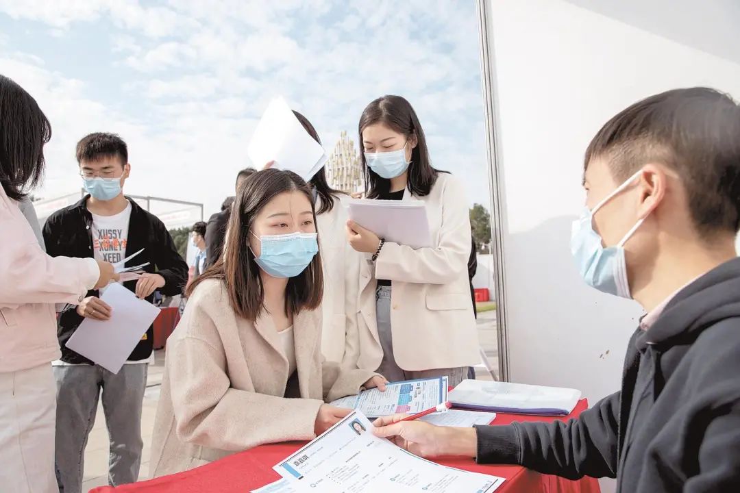 大学生在招聘会现场投递简历,与企业人员交流.