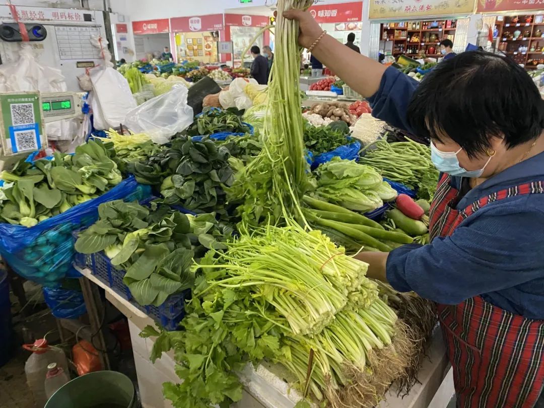 上午,在界泾港农贸菜市场内,蔬菜摊主特别忙碌,绿叶菜跌价,不少市民